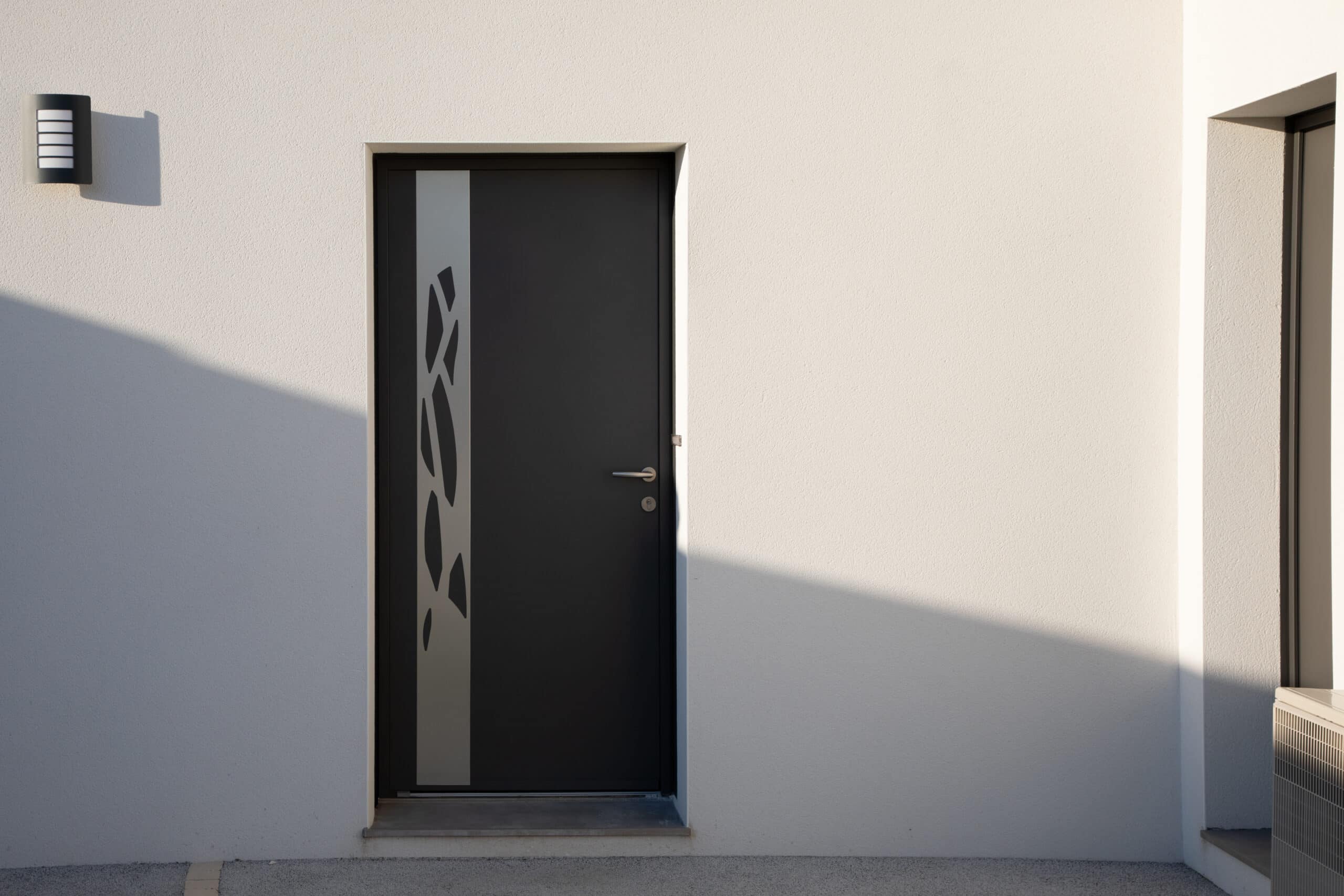 Porte d'entrée moderne design anthracite et façade blanche Façade moderne blanche avec porte d'entrée anthracite et motif abstrait. Applique murale design, fortes ombres solaires, unité de climatisation.