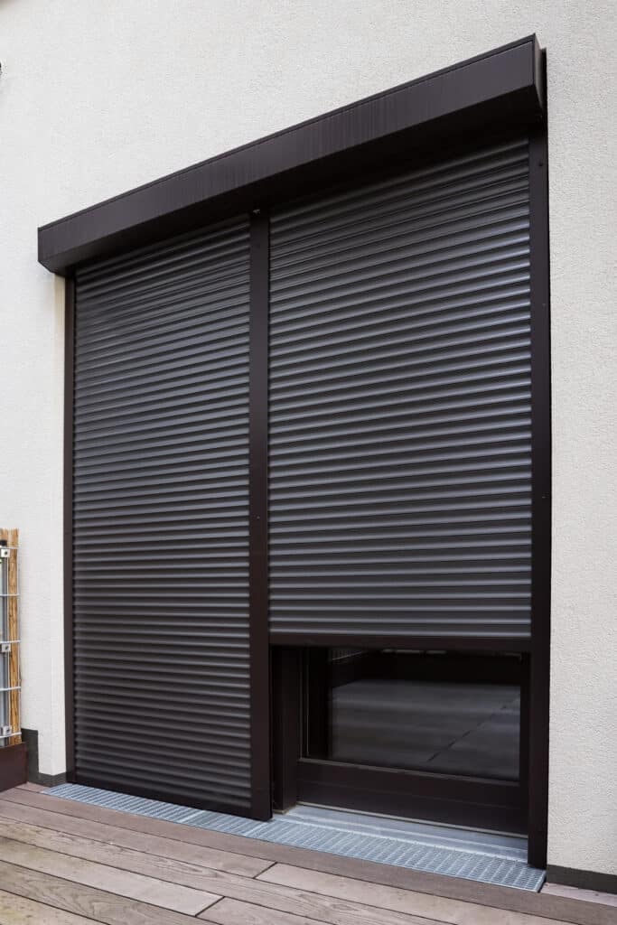 Volet roulant design pour porte-fenêtre moderne et terrasse bois Façade moderne avec volet roulant marron recouvrant une porte-fenêtre. Terrasse en bois et grille de drainage.